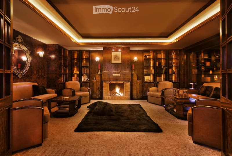 Elegant living room with a fireplace, leather sofas, armchairs, coffee tables, bookshelves, and a large fur rug.