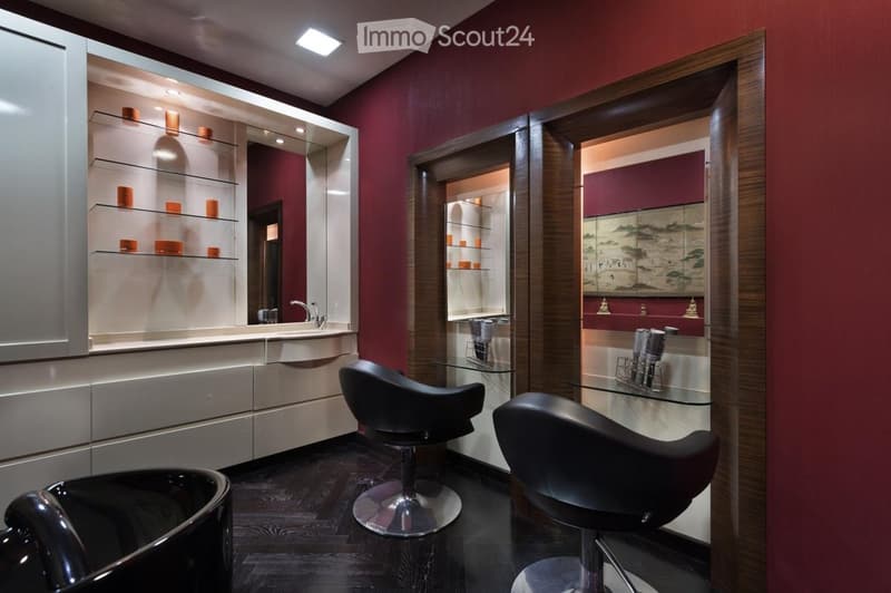 Modern bathroom with dark red walls, sleek white cabinetry, glass shelves, and three black stools. Features a large mirror, a sink with a modern faucet, and a glass table with two additional stools.