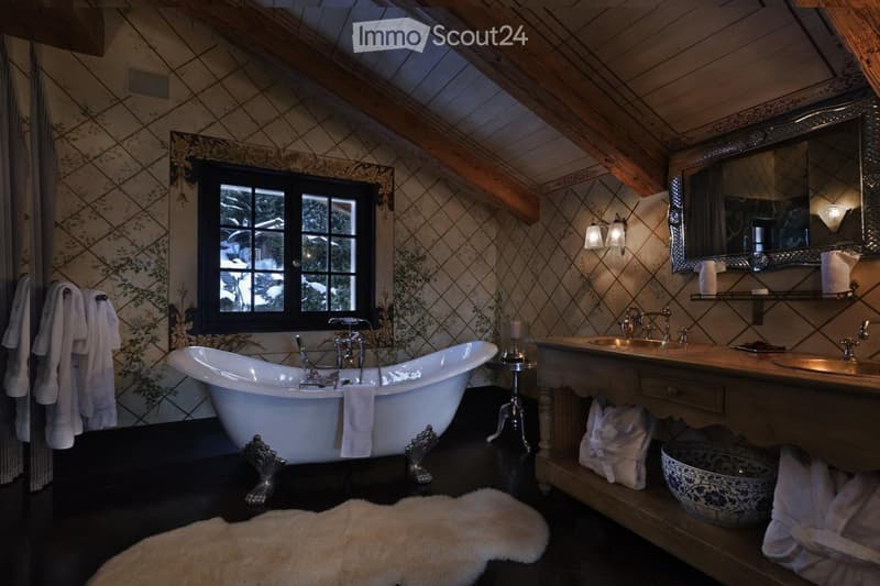 Elegant bathroom with a large clawfoot bathtub, double sink vanity, ornate mirror, and decorative towels. Exposed wooden beams and patterned tiles add warmth.