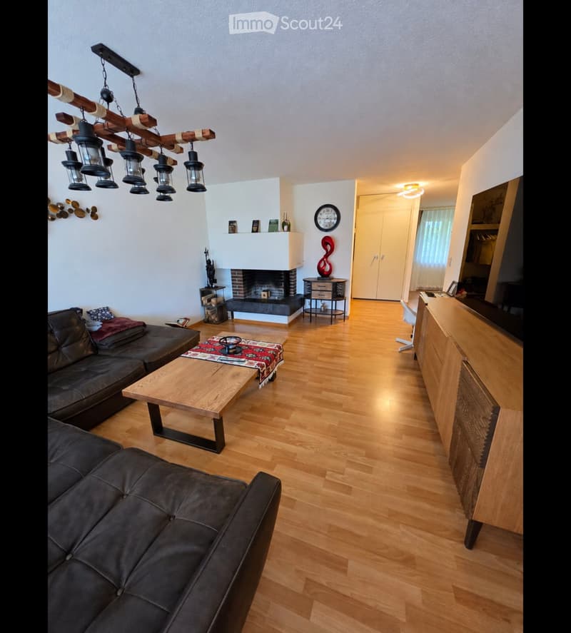 Modern living room with hardwood floors, a black leather sofa, a wooden coffee table, a fireplace, and a chandelier.