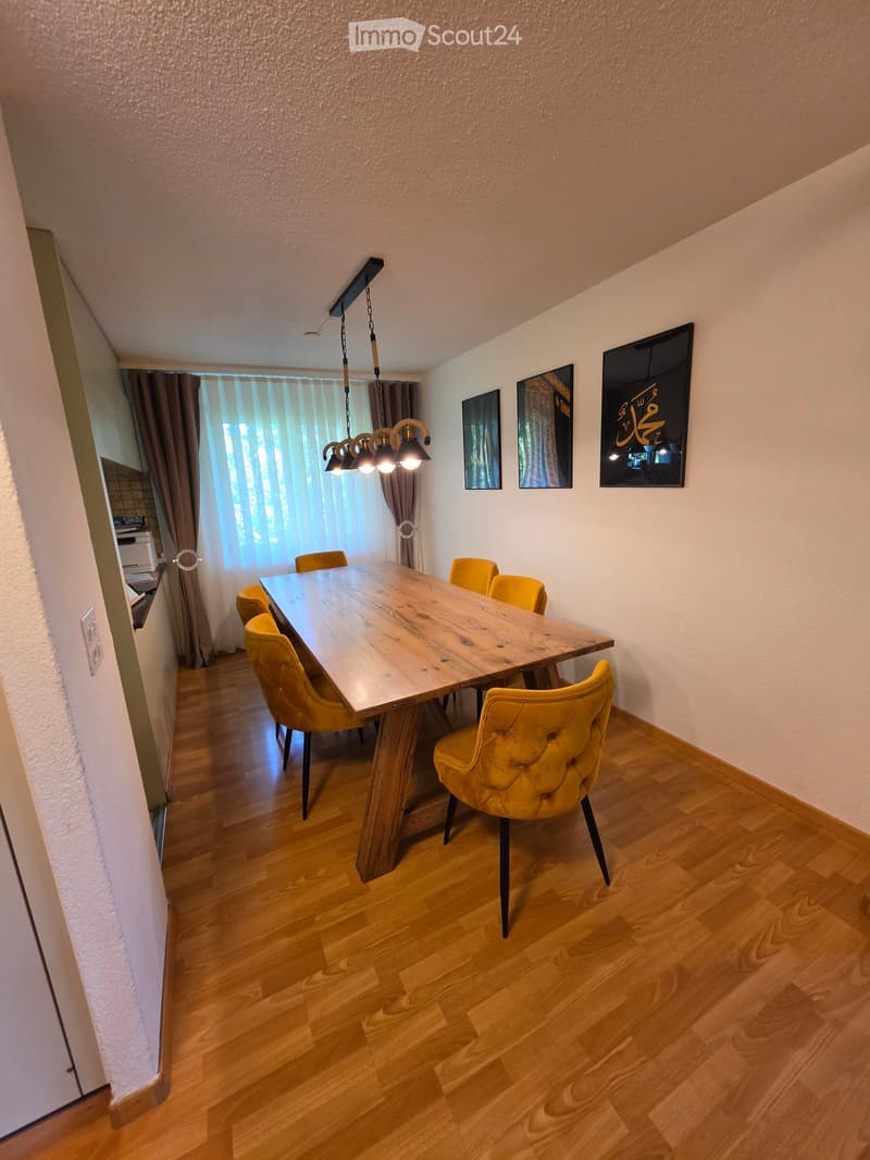 Dining room with wooden floor, large wooden dining table, yellow upholstered chairs, and modern lighting fixture.