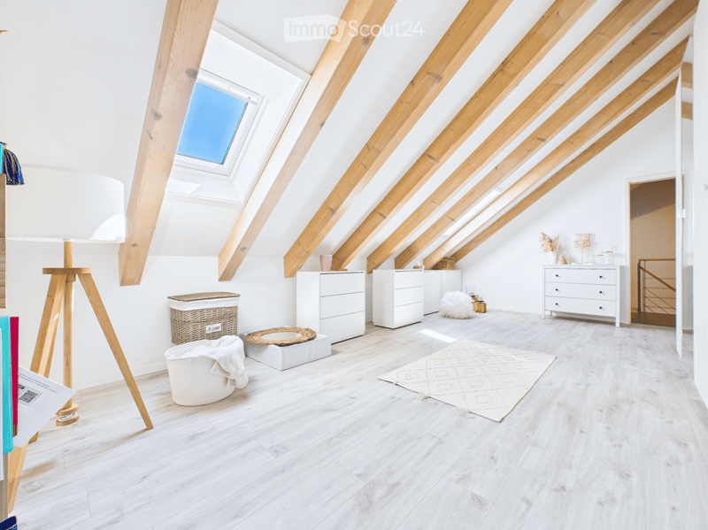 Bright, airy attic room with wooden beams and skylights. Features include a white floor lamp, wicker basket, white dresser, white cabinet, white rug, stool, and a mirror on the wall.