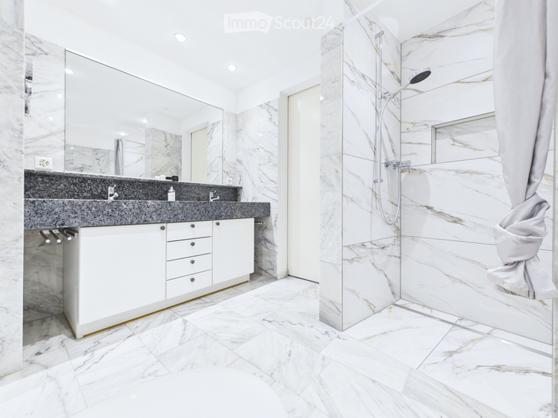 Modern bathroom with marble tiles, double sink, large mirror, and a walk-in shower with glass enclosure.