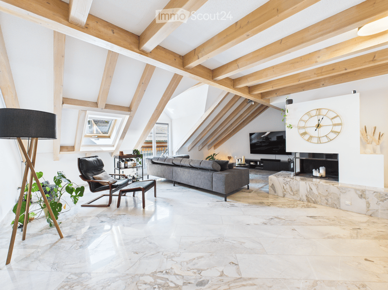 Modern living room with exposed wooden beams, large windows, grey sofa, armchair, coffee table, floor lamp, television, fireplace, and decorative clock.