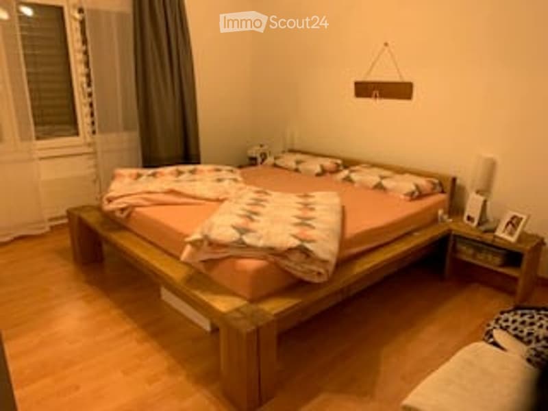 Cozy bedroom with wooden bed, pink bedding, nightstand with lamp, and a small picture frame on the nightstand.