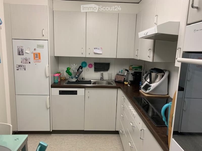 Modern kitchen with white cabinets, stainless steel appliances, and a dark wooden countertop. Includes a refrigerator, dishwasher, sink, microwave, toaster, coffee maker, and a small table with a stool.