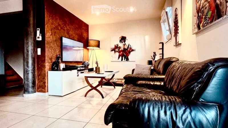 Modern living room with a dark leather sofa, a small wooden coffee table, a floor lamp, a TV on a white stand, and decorative art pieces on the walls.