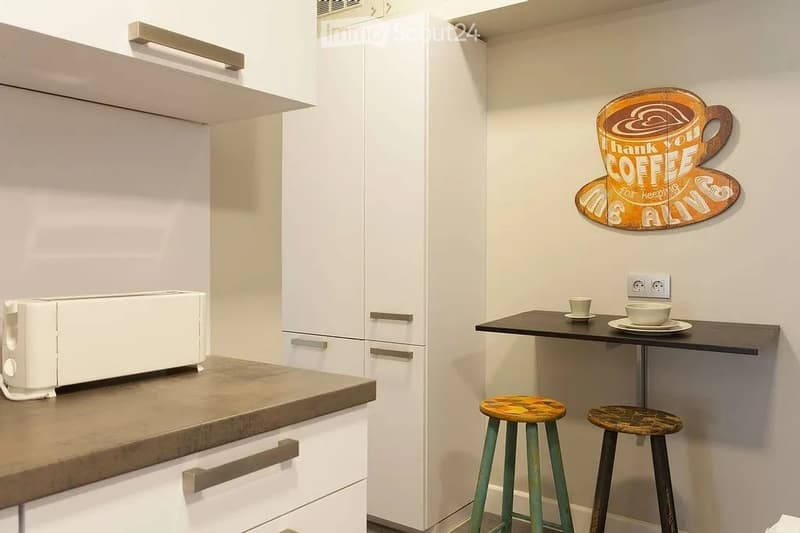 Modern kitchen with white cabinets, a countertop, a toaster, and a small dining area with two stools and a table.
