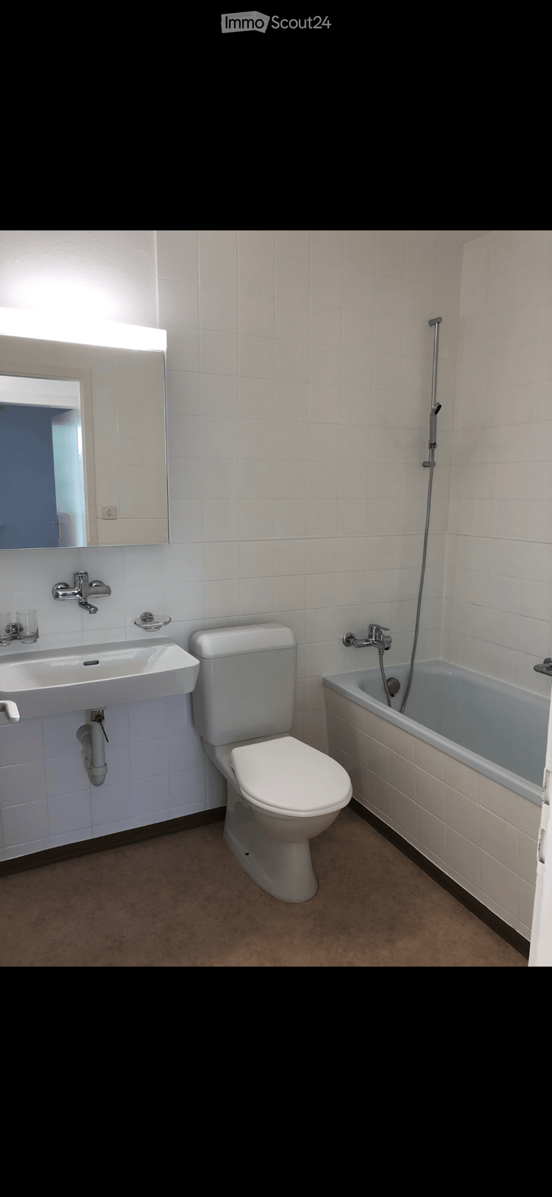 Modern bathroom with white tiles, a sink, toilet, bathtub, and a mirror above the sink.