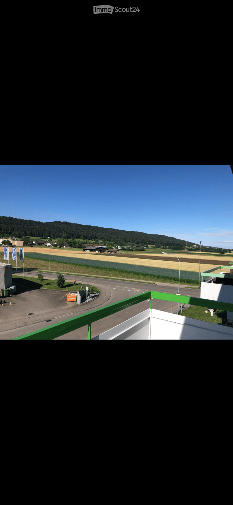 Balcony overlooking a parking lot, road, and rural landscape with fields and hills in the background.