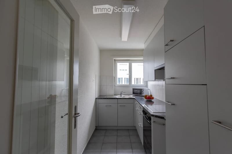 Modern, compact kitchen with white cabinets, a sink, microwave, oven, and a fruit bowl on the counter.