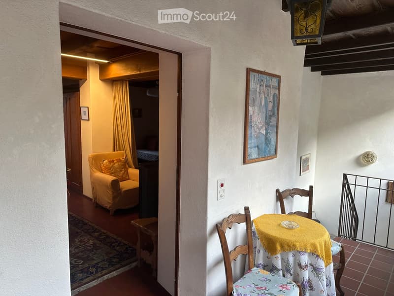 Cozy living area with a yellow sofa, wooden chairs, small table with a yellow cloth, and artwork on the wall.