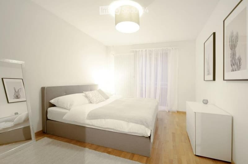 Modern bedroom with a grey upholstered bed, white bedding, a nightstand, a mirror, and picture frames on the walls.