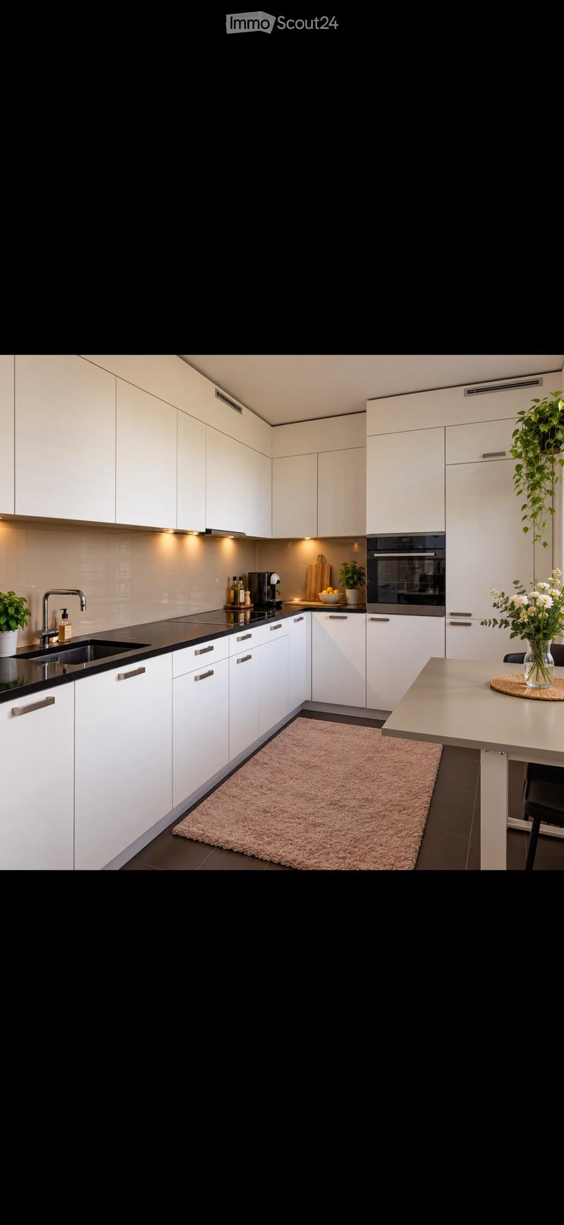 Modern kitchen with white cabinets, black countertops, stainless steel sink, built-in oven, coffee maker, and decorative plants.
