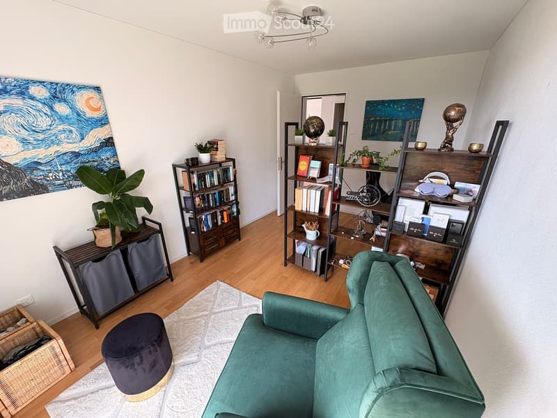 A modern living room with a green velvet sofa, a round dark blue stool, multiple bookshelves filled with books and decorative items, a large painting of The Starry Night, and a potted plant on a side table.