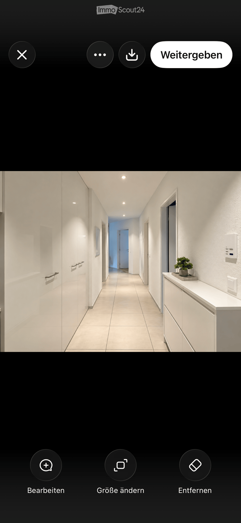 Modern hallway with white walls, tiled floor, recessed lighting, and a small plant on a cabinet.