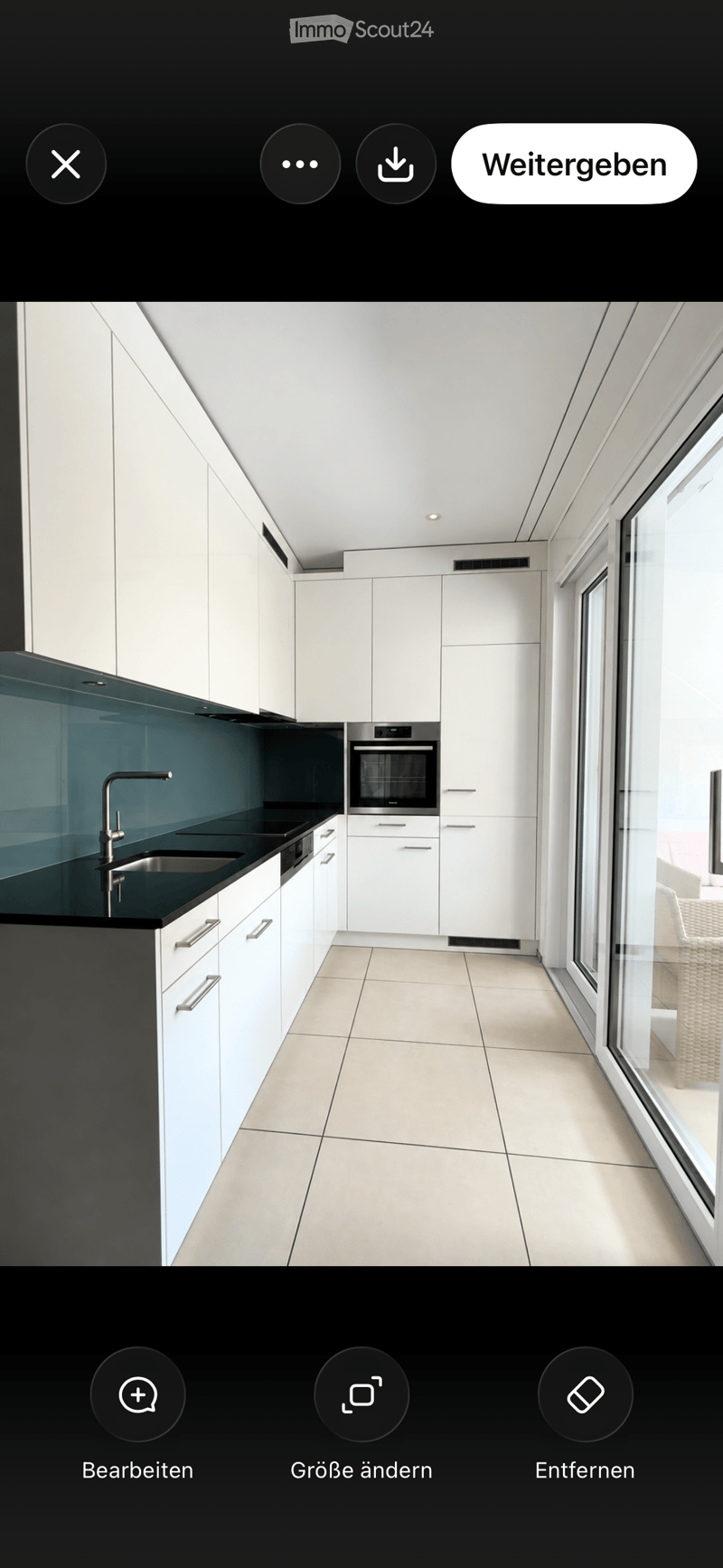 Modern kitchen with white cabinets, black countertops, stainless steel appliances, and large windows.