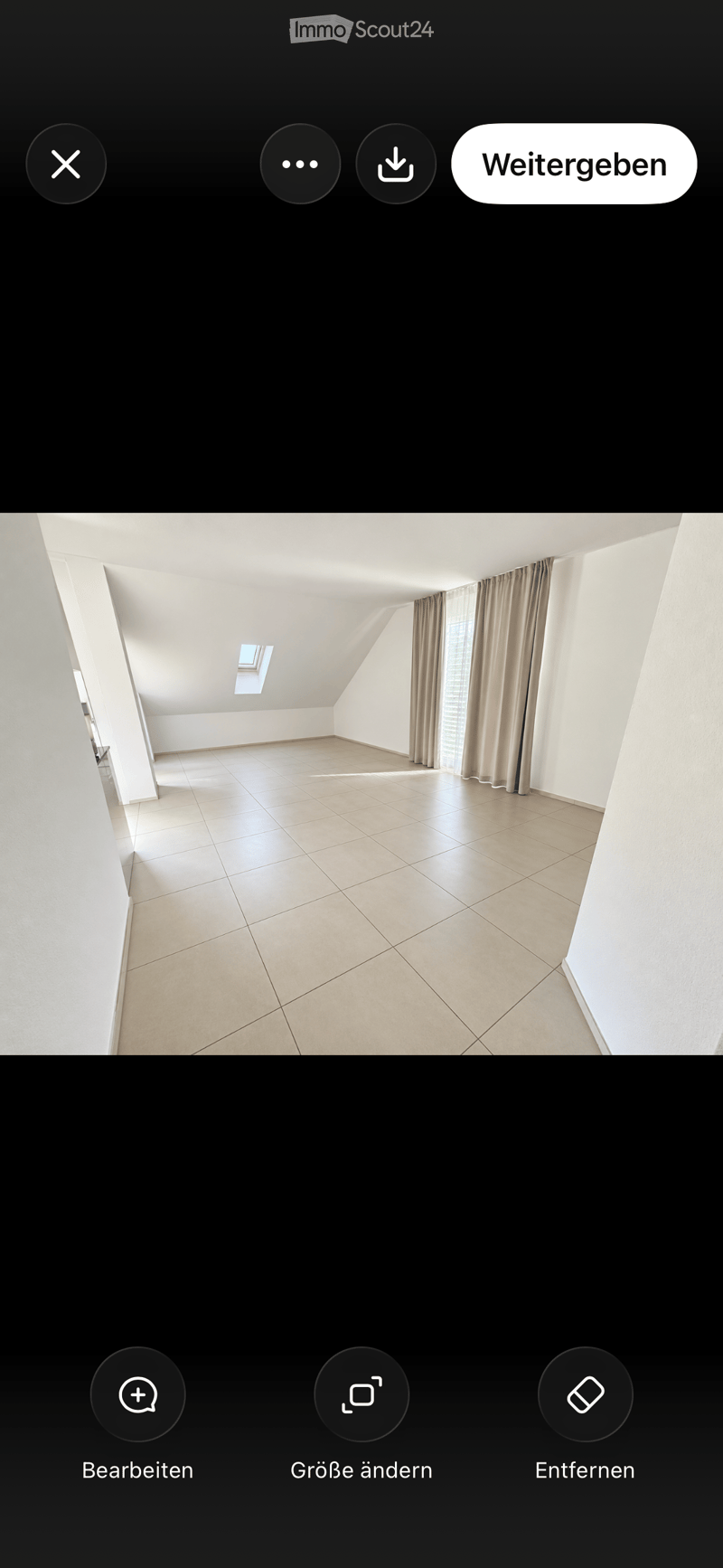 Empty attic room with tiled floor, white walls, skylight window, and beige curtains on a window.