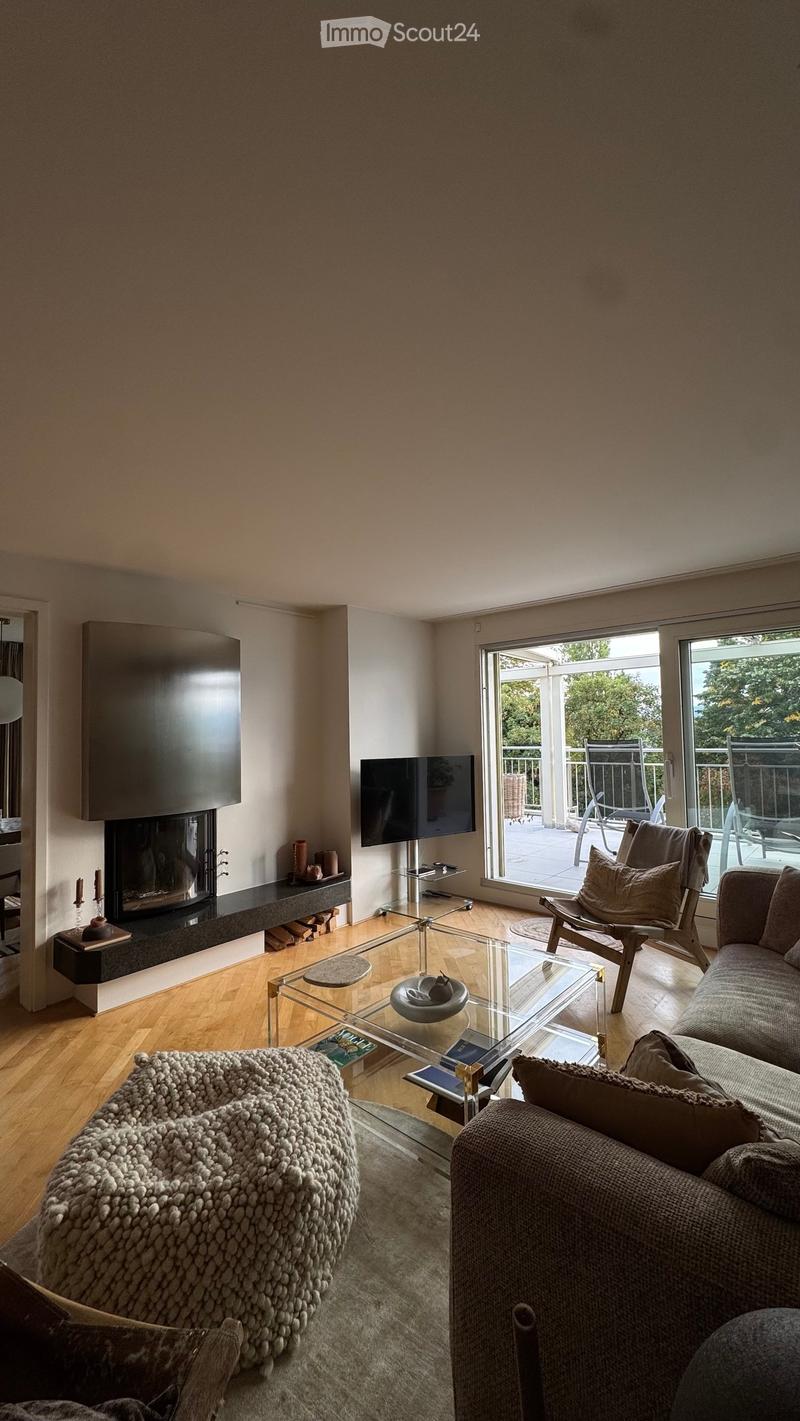Modern living room with a grey sofa, glass coffee table, fireplace, and large windows opening to a balcony.