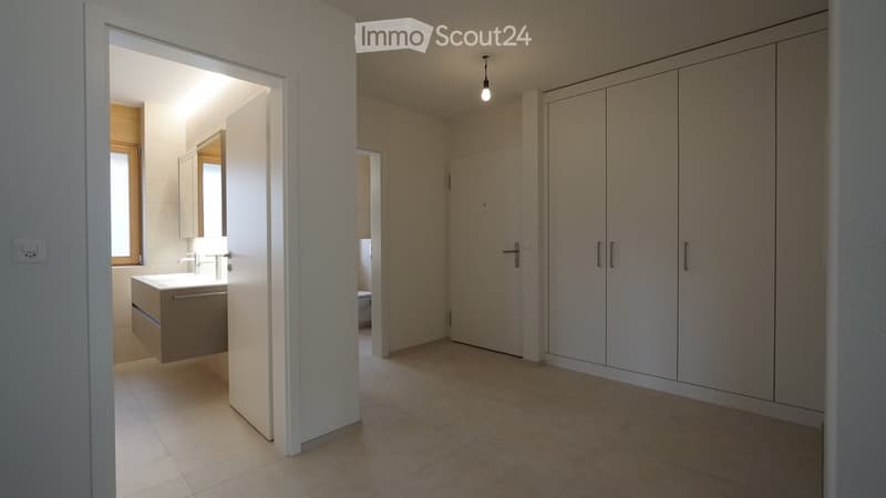 Empty room with tiled floor, white walls, built-in wardrobes, and an open doorway leading to a modern bathroom with a sink and mirror.