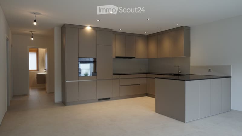 Modern kitchen with grey cabinets, a central island, and a sink area. The space features recessed ceiling lights and a tiled floor.