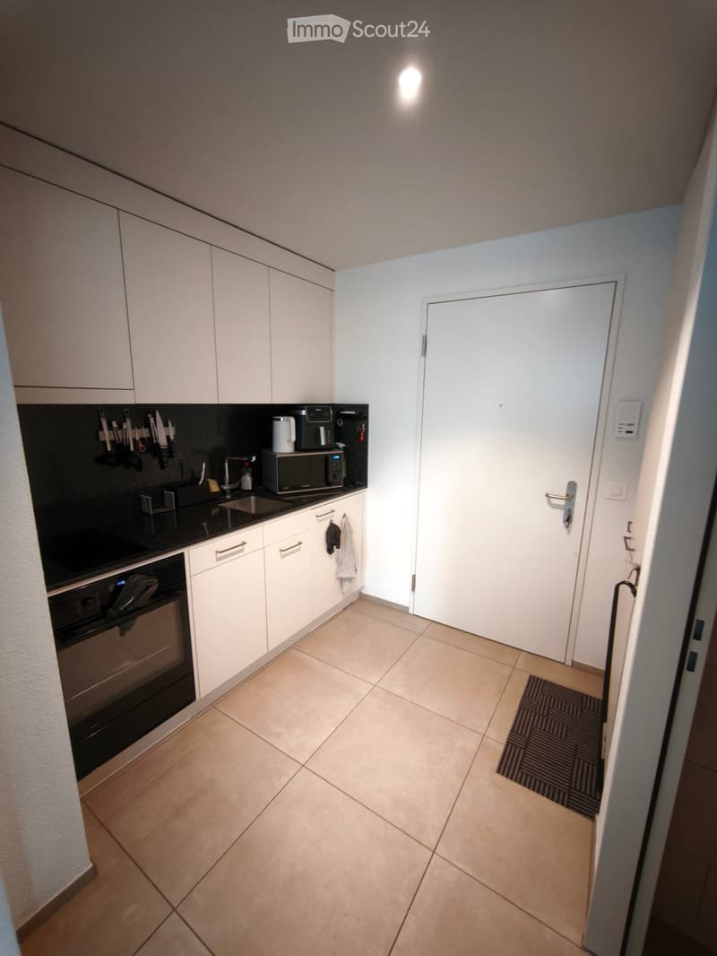 Modern kitchen with white cabinets, black countertop, stainless steel oven, microwave, and sink. Knife rack and coffee maker visible on countertop.