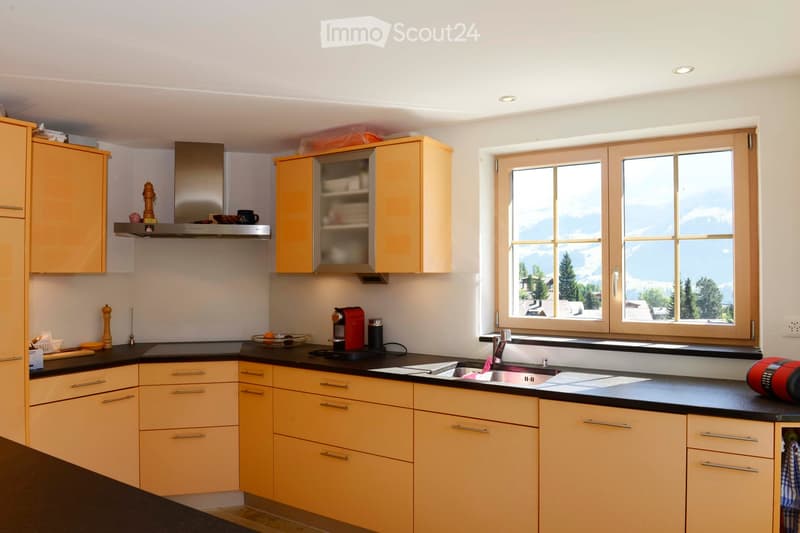 Modern kitchen with light wood cabinets, stainless steel appliances, and a large window offering a scenic mountain view.