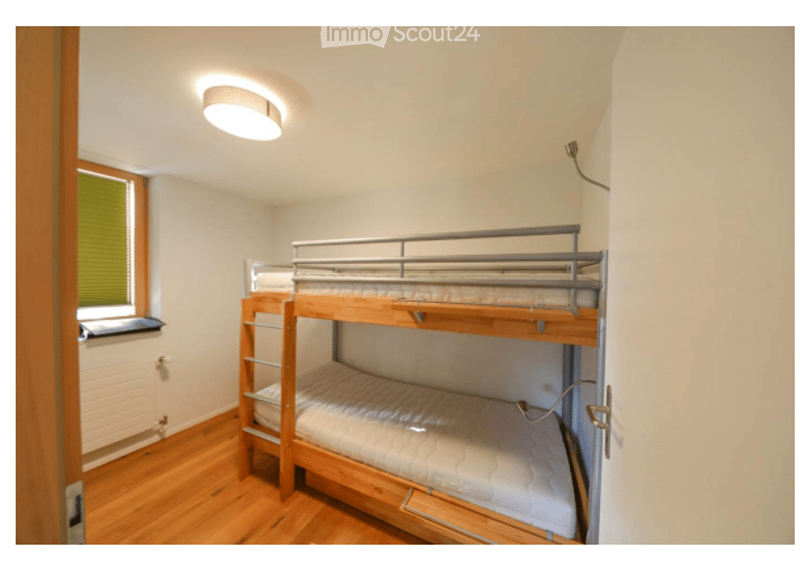 Cozy bedroom with a wooden bunk bed, white walls, wooden flooring, and a window with blinds.