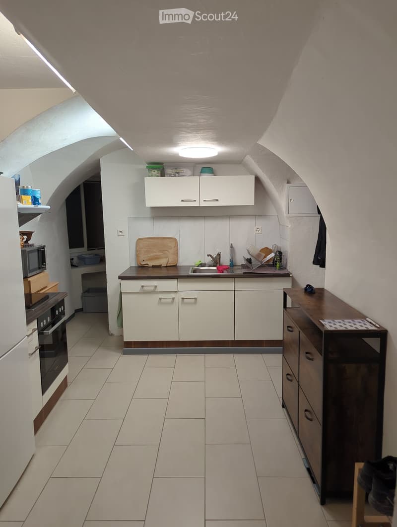 Modern kitchen with white cabinets, a dark countertop, and tiled flooring. Includes a refrigerator, oven, microwave, sink, and various kitchen items on the counter.