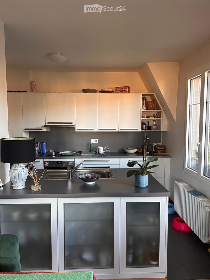 Modern kitchen with white cabinets, dark countertops, and stainless steel appliances. Features a sink, oven, and decorative lamp on the counter.