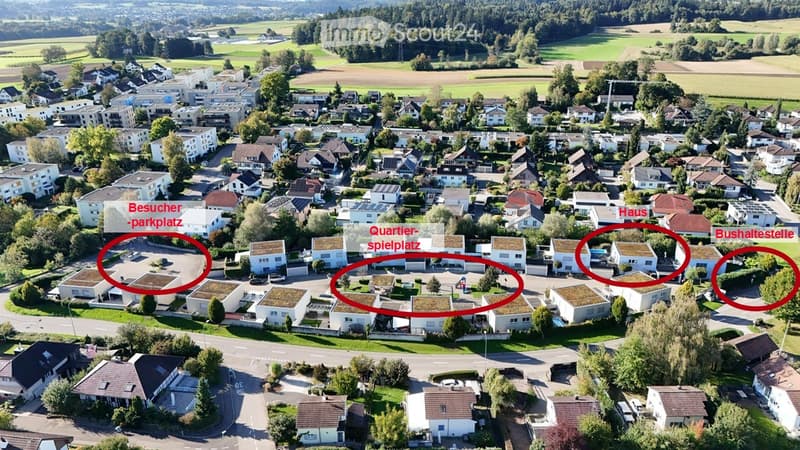 Aerial view of a residential neighborhood with multiple houses, green spaces, and a parking area.