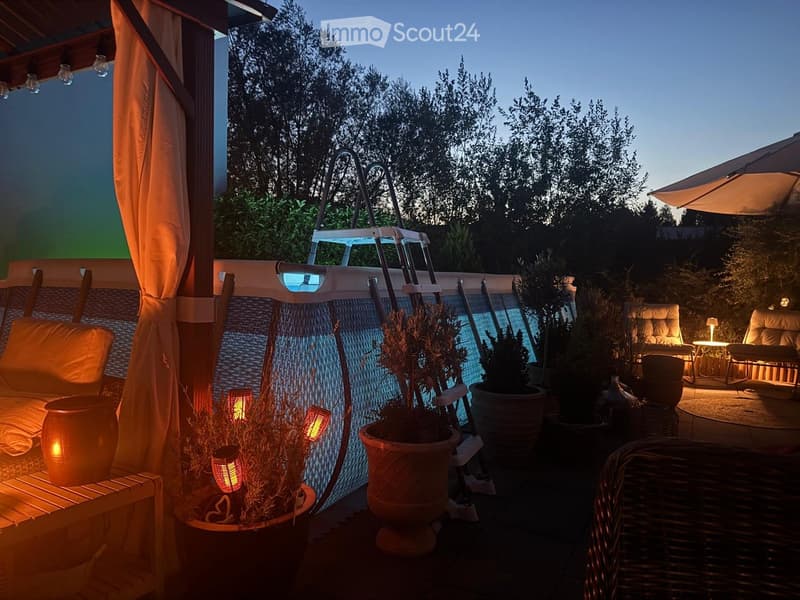 Evening outdoor patio with a small swimming pool, lounge chairs, potted plants, and ambient lighting.