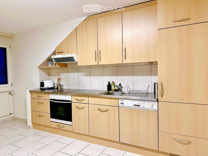 Modern kitchen with light wood cabinets, stainless steel appliances, and a tiled floor.