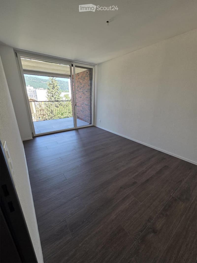 Empty room with dark wooden flooring, white walls, and large sliding glass doors leading to a balcony with a view.