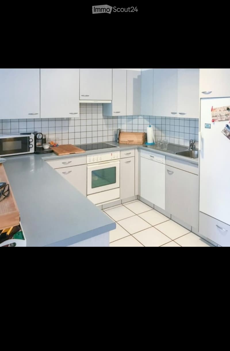 Modern kitchen with white cabinets, stainless steel appliances, and a light grey countertop. Features include a refrigerator, oven, microwave, sink, and dishwasher.