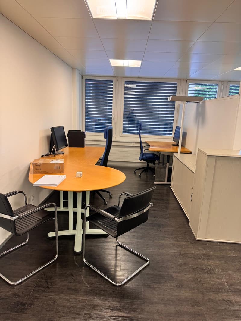 Office space with a round table, chairs, computer screens, and a cabinet.