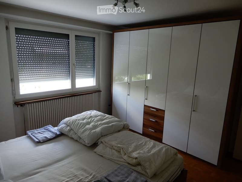 Bedroom with a neatly made bed, white wardrobe with mirrored doors, and a radiator beneath the window.