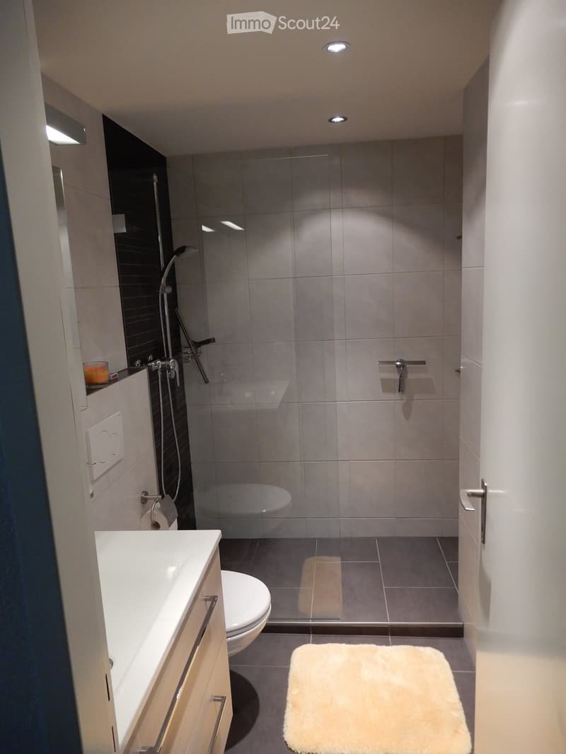 Modern bathroom with a white sink, toilet, bathtub, and a glass-enclosed shower area. Features a white bathroom rug, a mirror, and a sleek faucet.