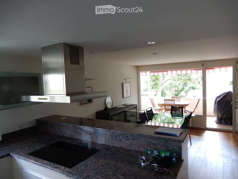 Modern kitchen with granite countertops, built-in stove, and a dining area leading to a balcony with outdoor furniture.