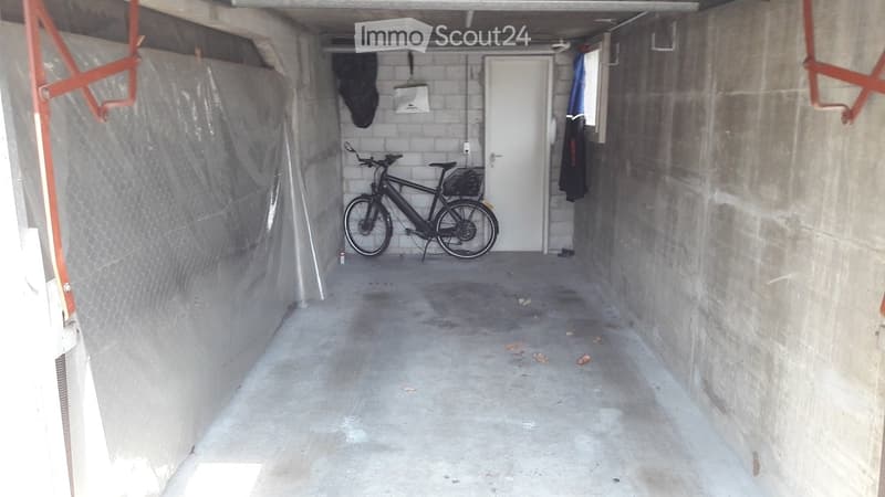 Concrete garage with a bicycle parked inside, a white door at the back, and some protective coverings on the walls.