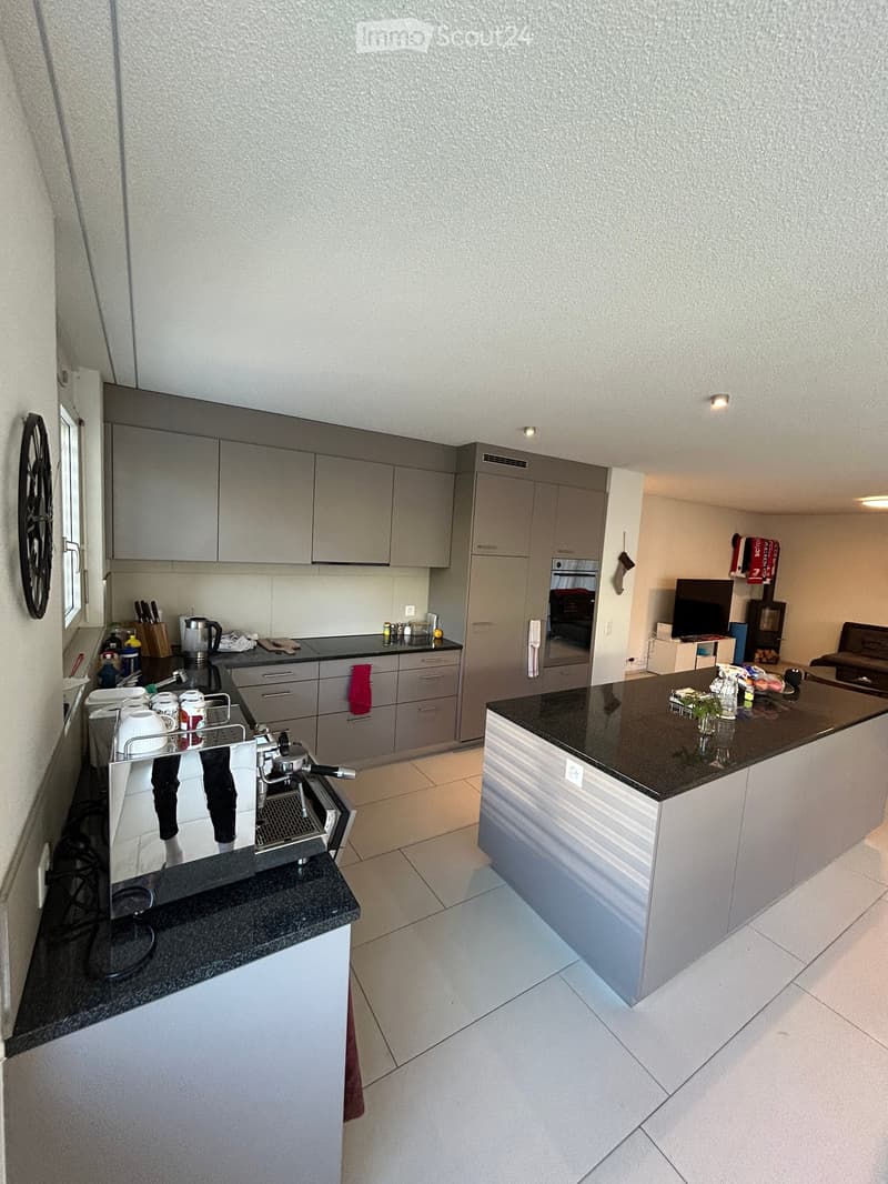 Modern kitchen with grey cabinets, black countertops, and stainless steel appliances. Includes a coffee machine, oven, sink, and various kitchen items on the counters.