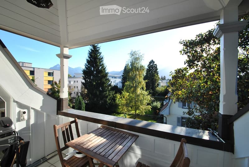 Balcony with wooden table and chairs, overlooking a scenic view of trees and mountains.