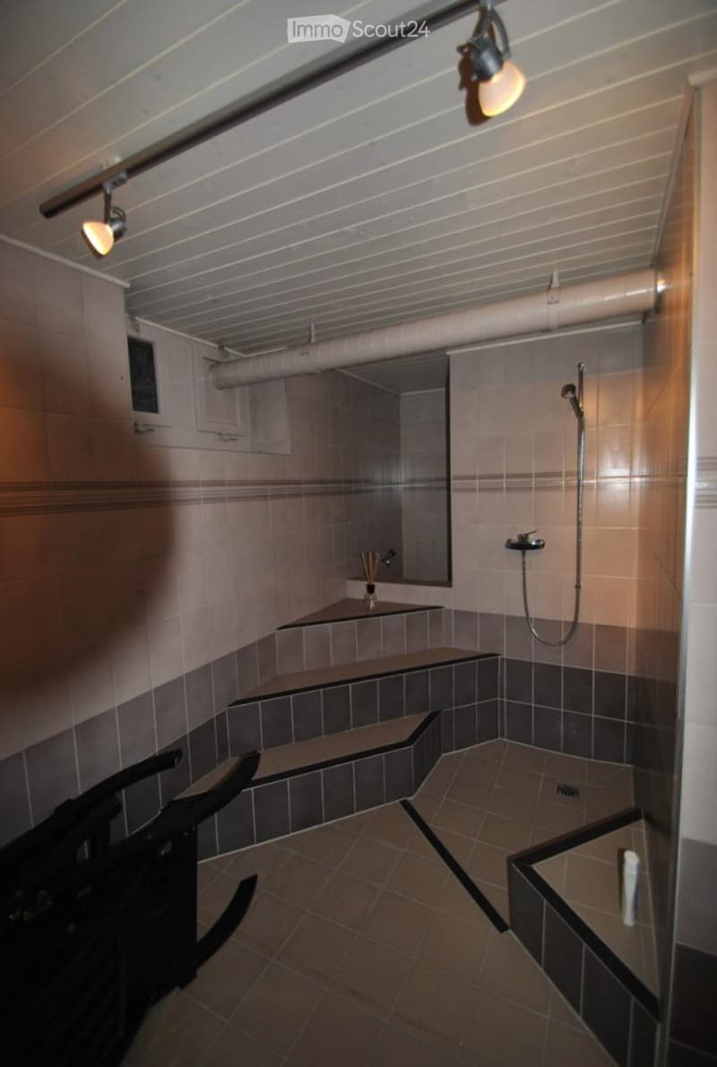 Modern bathroom with tiled walls and floor, built-in benches, a shower area, and a mirror above a small shelf.