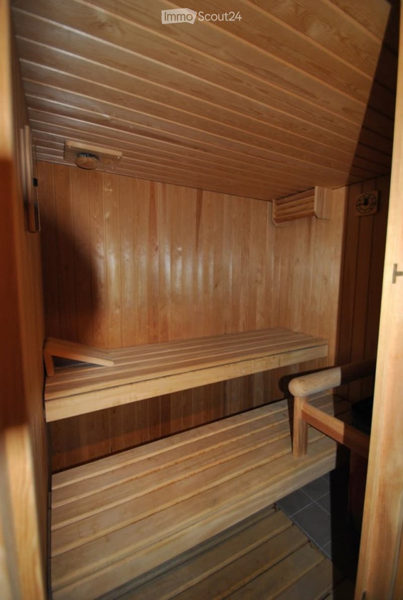 Wooden sauna with multiple wooden benches and a small control panel on the wall.