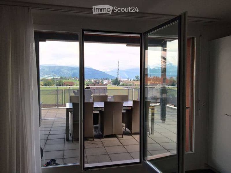 Balcony with a view of a green field and mountains, featuring a dining table and chairs.