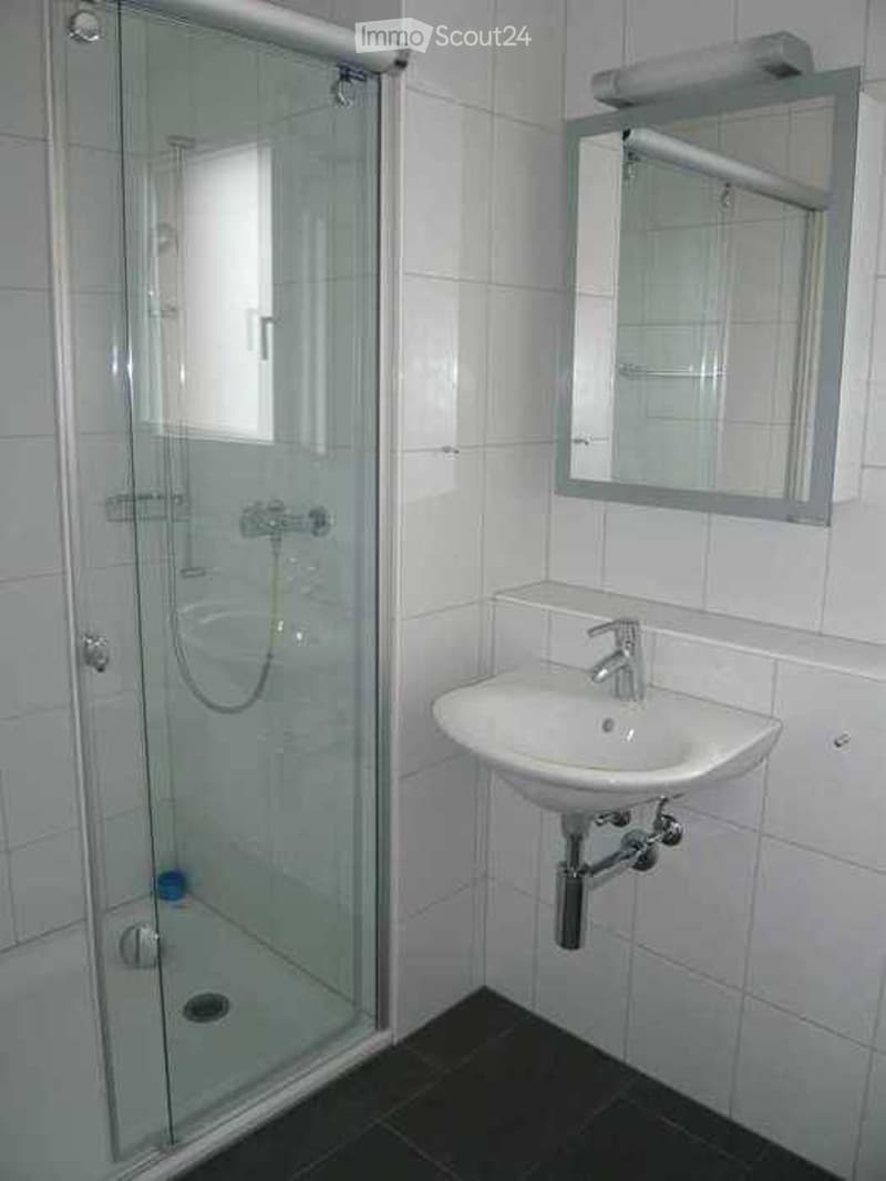 Modern bathroom with white tiles, a glass-enclosed shower, a white sink with a chrome faucet, and a mirror above the sink.