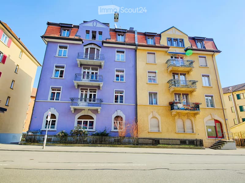Two colorful apartment buildings with multiple windows and balconies, featuring vibrant purple and yellow facades and red-tiled roofs.