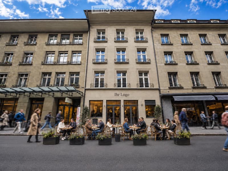 A multi-story building with large windows and balconies, featuring a restaurant with outdoor seating on the sidewalk.