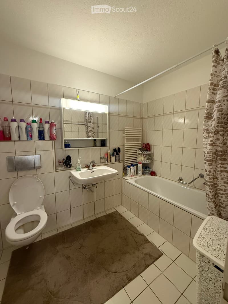 Bathroom with a toilet, sink, bathtub, mirror, and various toiletries. Includes a towel rack, shower curtain, and a laundry basket.