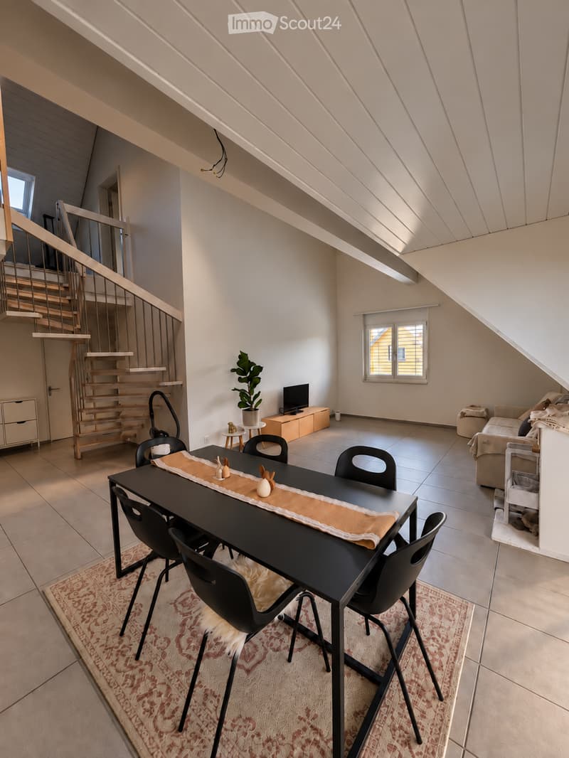 Bright, open living and dining area with a black dining table, six chairs, a sofa, a television, a plant, and a staircase leading to an upper level.